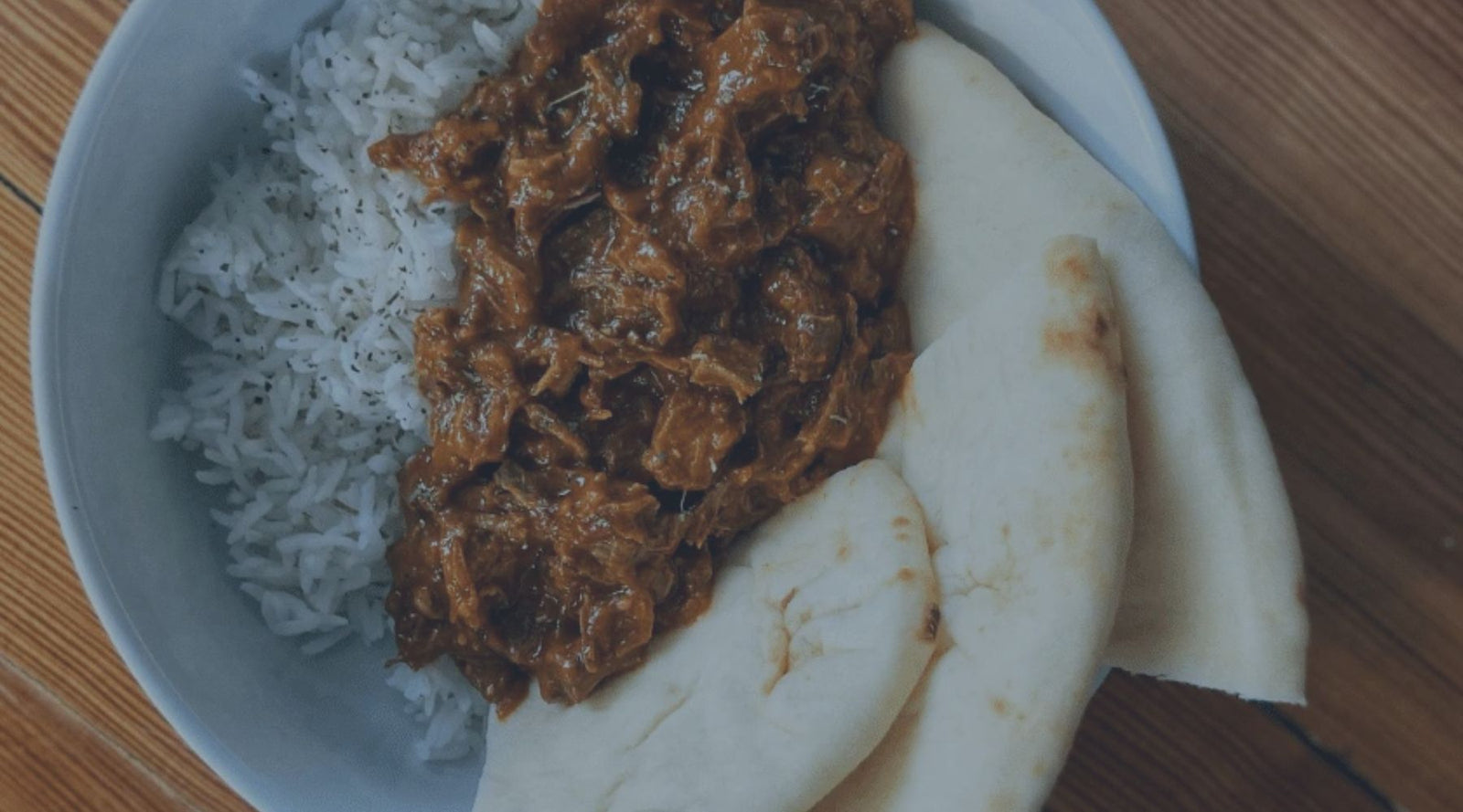 goat curry in a white bowl with rice and naan