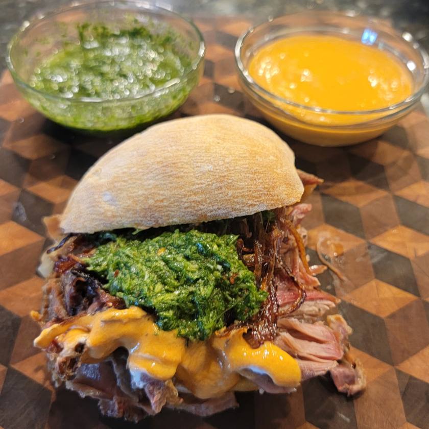 Shredded BBQ goat sandwich on cutting board with two bowls of sauces