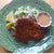 breaded goat schnitzel with potato salad and gravy on a green plate.