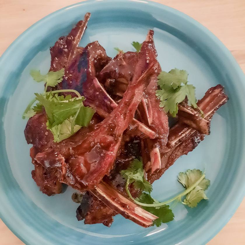 Braised goat chops stacked on a blue plate with cilantro 