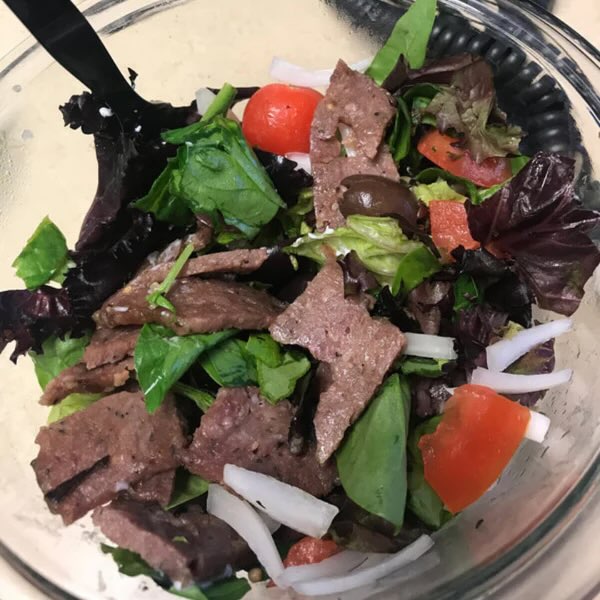 goat gyro salad with onion, tomato and olives in a glass bowl